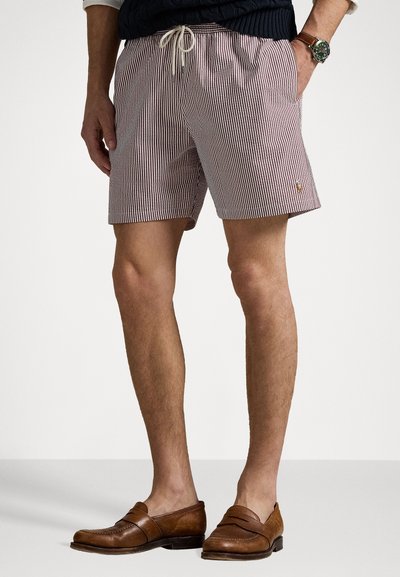 Herre svømshorts med striber i røde og hvide vertikale striber, elastisk talje med snor og to side lommer. Brun læder loafers er iført.