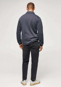 Maglione a maglia blu navy con piccolo colletto, abbinato a jeans grigio scuro e sneakers chiare. La texture sembra morbida, con un design a vestibilità rilassata.