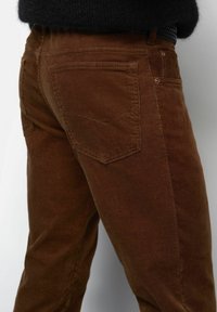 Close-up of a person wearing brown corduroy pants with back and side pockets, paired with a black belt and dark top.