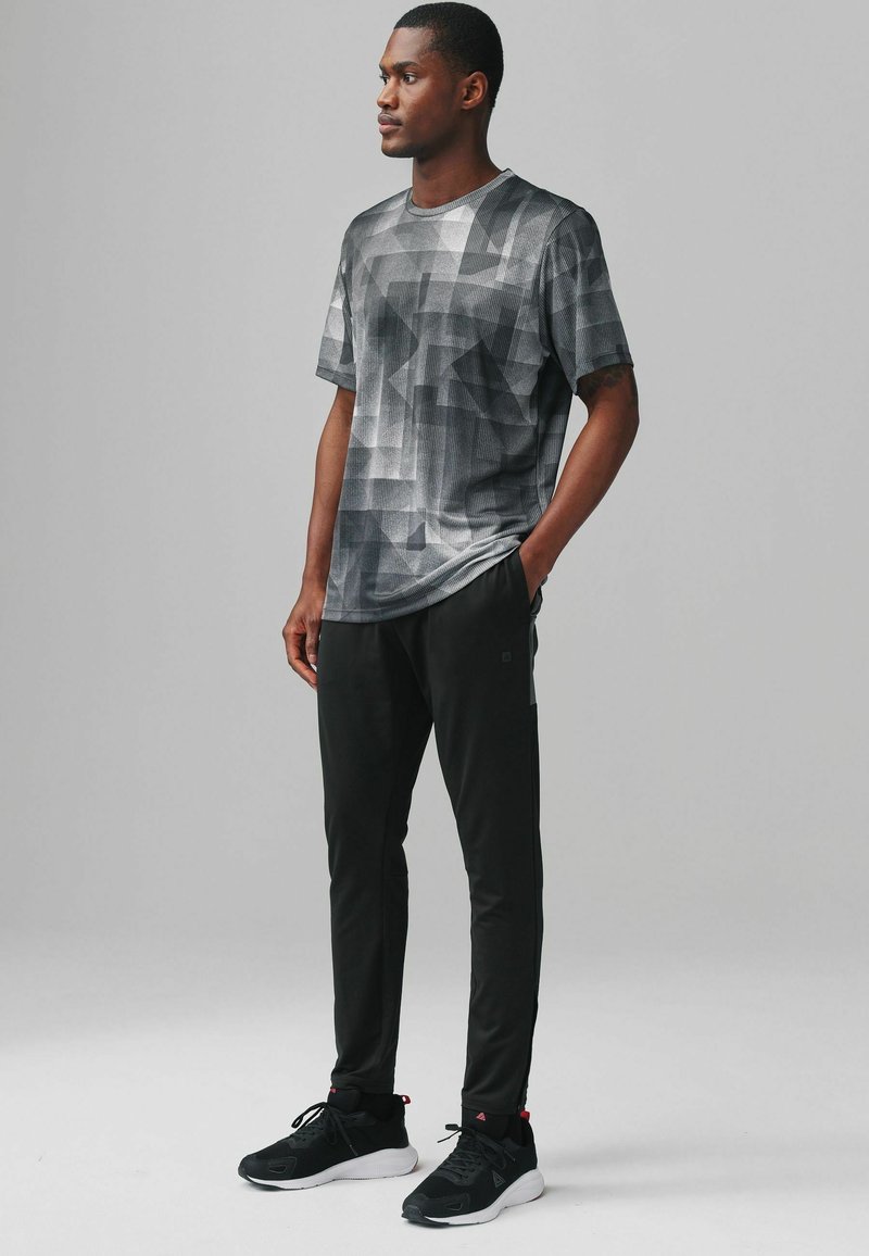 Gray geometric patterned t-shirt paired with black athletic pants and black sneakers, featuring a relaxed fit and smooth texture.