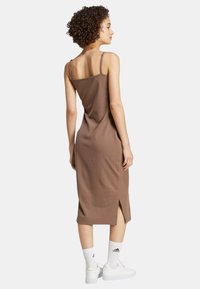 Abito midi marrone a costine con spalline sottili, strappo laterale e design elegante, abbinato a sneaker bianche e calze fino al ginocchio.