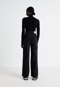 Crna turtleneck džemper od cable-knita u kombinaciji s crnim cargo hlačama visokog struka s bočnim džepovima i opuštenim krojem, uz ravne cipele.