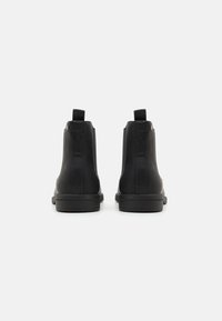 Botas de tobillo de cuero negro con una textura suave, que cuentan con un tirador en la parte trasera y un diseño de punta redonda, montadas sobre una suela negra robusta.