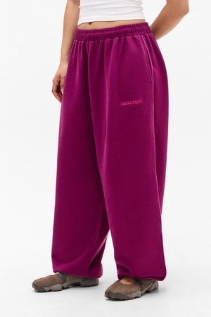 Person wearing loose, bright purple sweatpants with elastic waistband, side pockets, and brown slip-on shoes, standing against white background.