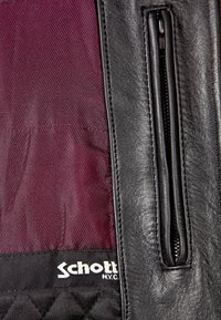 Černá kožená bunda s prošívanou vínovou podšívkou, zipovou kapsou a bílým logem značky na spodním okraji. Hladká textura a přizpůsobený střih.
