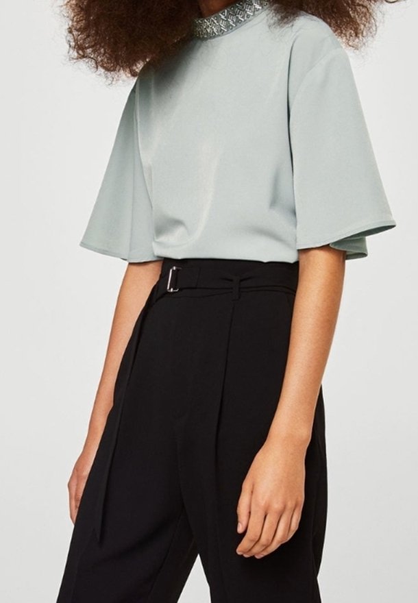 Top azzurro chiaro a maniche corte con colletto alto e cuciture decorative, abbinato a pantaloni neri a vita alta con cintura.