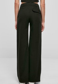 Vida byxor i mörk olivgrön, tillverkade av bomull. Har en bakficka med knappdetalj och en hög midjedesign. Slät textur.