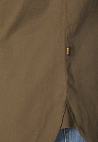 Koszulka w oliwkowym kolorze wykonana z mieszanki bawełny, charakteryzująca się subtelną teksturą, bocznymi rozporkami oraz małą metką logo BOSS przy dolnym brzegu.