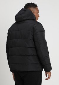 Sort pufferjakke med hætte, der har quilted syninger og en glat, skinnende overflade. Designet er firkantet med en afslappet pasform.
