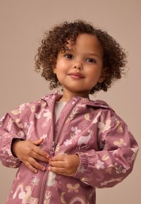 Veste pour enfants rose clair présentant un motif fantaisiste d'unicornes, de fleurs et de papillons ; tissu texturé et fermeture éclair.