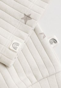 Close-up of cream-colored ribbed fabric with small gray star prints and white tags featuring a gray rainbow logo.