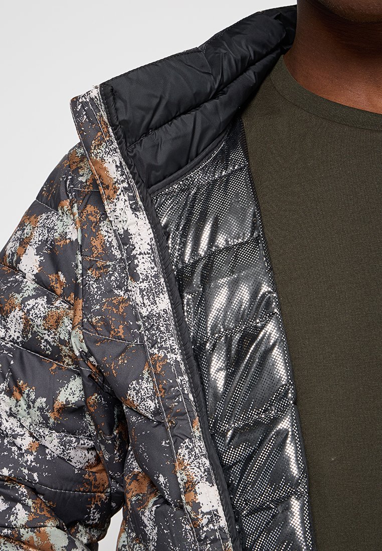 Kurtka ocieplana w czarno-brązowy abstrakcyjny wzór. Posiada błyszczące srebrne podszycie i czarny kołnierz. Pod spodem widoczna bawełniana koszula.