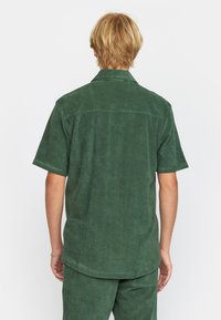 Groen kortemouwen shirt van zacht stof met een geprofileerde afwerking, met een kraag en een ontspannen pasvorm. Achteraanzicht toont eenvoud in het ontwerp.