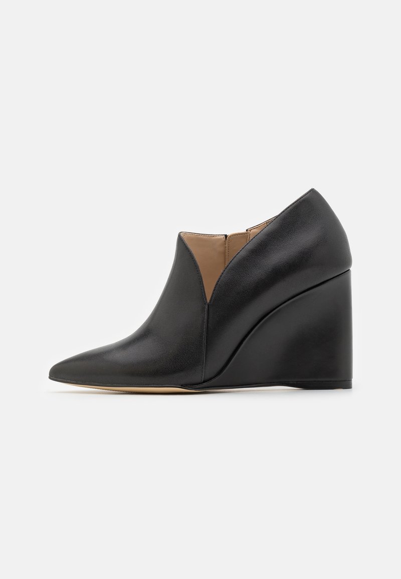 Bottines compensées en cuir noir avec un bout pointu, présentant un design en V prononcé et un intérieur beige. Texture lisse et silhouette épurée.