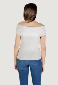 Top bianco a costine con design aderente e maniche corte, abbinato a jeans blu con tasche posteriori e vestibilità affusolata.