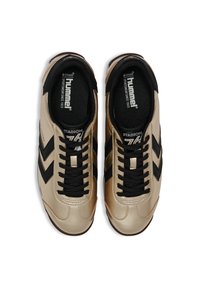 Ett par beige och svarta Hummel Stadion 76 sneakers med svarta snören, chevron-logostripes och vadderade svarta innersulor.