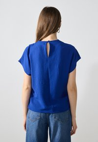Top blu corto a maniche corte con finitura testurizzata, presenta un dettaglio a occhiello sul retro ed è abbinato a pantaloni di jeans a vita alta.