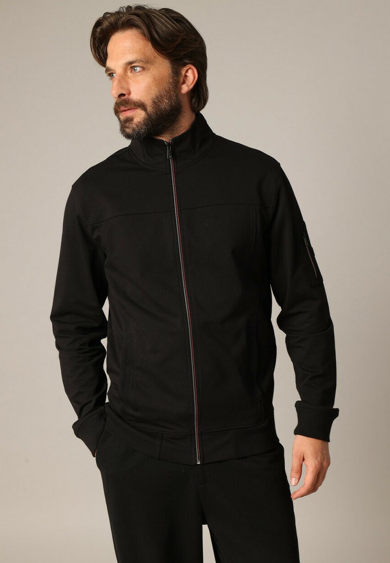 Zwarte zip-up jasje met hoge kraag, voorzien van rode en witte accentsteken, zijzakken en geribbelde manchetten. Gladde stoftextuur.