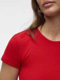 Nahaufnahme einer Person, die ein rotes, geripptes Kurzarmshirt und Creolen trägt, wobei ein Teil von Hals, Schulter und Haar sichtbar ist.