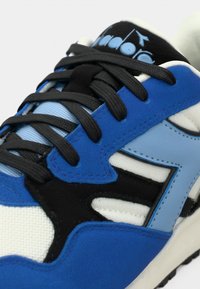 Αθλητικό παπούτσι από μπλε σουέτ και δίχτυ με μαύρα κορδόνια, λευκή και ανοιχτό μπλε διακοσμητική επικάλυψη και λαστιχένια σόλα για πρόσφυση.