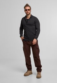 Grau ZIP-Pullover, dunkelbraune Cargo-Hosen, beige Stiefel; Merkmale sind lange Ärmel, Seitentaschen und ein strukturiertes Material.