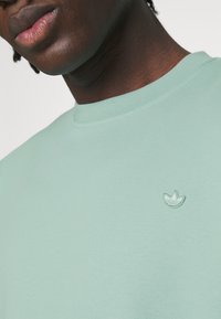 Mintgrön sweatshirt i mjukt tyg, med en ribbad rund nacke och en liten broderad logotyp på bröstet.