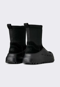 Stivaletti neri alla caviglia con una combinazione di tessuto strutturato e gomma liscia, suola spessa e linguette laterali per facilitare la calzata.