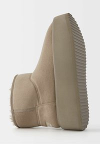 Krémově hnědá semišová kotníková bota s texturovanou gumovou podrážkou, s zaobleným tvarem a hřejivým detailním manžetou z umělé kožešiny.