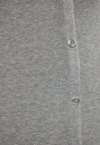 Cardigan grigio in tessuto a coste, con bottoni argentati lungo la parte frontale, con una texture morbida e un design aderente.