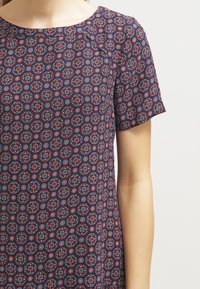 Top a maniche corte stampato con una base blu navy e motivi geometrici rossi e blu. Tessuto morbido con scollatura rotonda e vestibilità comoda.
