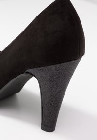 Chaussure à talon haut en cuir nubuck noir avec un talon en paillettes texturé, une forme effilée et une doublure intérieure lisse.