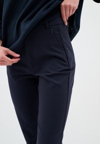 Námořnické modré kalhoty vyrobené z hladké, elastické tkaniny. Obsahují kapsu na zip a elegantní design s upraveným střihem.