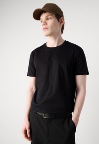 Black t-shirt made of cotton, round neck, short sleeves, paired with black trousers and a brown cap with embroidered logo, minimalistic design.
