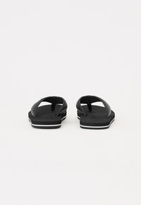 Svarte flip-flops med gummisåler, teksturerte stropper og hvite akksentlinjer langs kanten. Åpen tå-design med en enkel, flat stil.