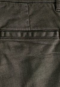 Pantalones de tela verde oscuro con un acabado texturizado. Cuentan con una cinturilla lisa y un único bolsillo trasero con un borde cosido.
