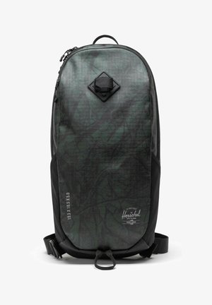 Sac à dos vert foncé avec une surface texturée et à motifs. Doté d'une poche en losange noire et de poches latérales en maille noire. Fermeture éclair.