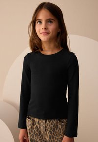 Top negro de manga larga con textura acanalada y escote redondo, combinado con pantalones de estampado de leopardo en marrón claro. Textura suave, diseño ajustado.