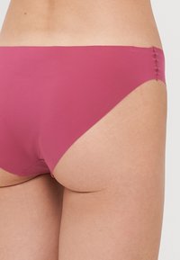 Parte inferiore di bikini rosa con una superficie liscia e opaca, caratterizzata da un design a vita bassa e cuciture pulite lungo i bordi.