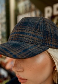 Dunkelblaue Wollmütze mit braunem Karomuster. Verfügt über eine abgerundete Krempe und eine strukturierte Oberfläche. Geeignet für die Freizeit.