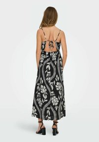Zwarte maxi-jurk met wit bloemenpatroon, voorzien van verstelbare spaghettibandjes, een open rug met strikdetail en een ontspannen pasvorm.