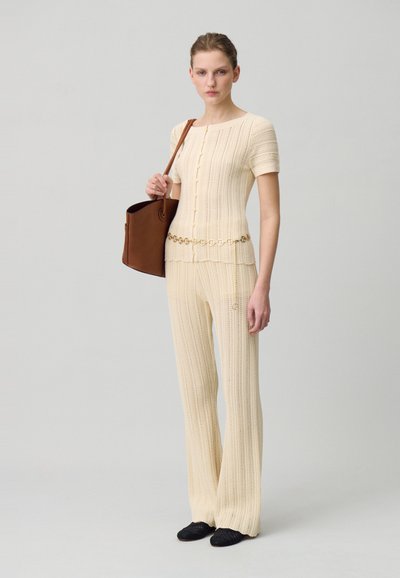 Débardeur en tricot léger avec des manches courtes et des boutons, associé à un pantalon large assorti. Accessoirisé avec un sac marron et des chaussures noires.