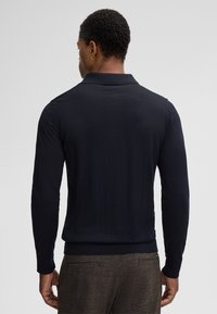 Marineblauwe polo met lange mouwen, voorzien van een geribbelde kraag en manchetten, met een slim fit ontwerp en een zachte stofstructuur. Achteraanzicht weergegeven.