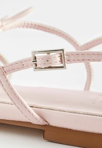 Dame rosa lædersandal med tynde stropper, en metallisk spænde og en flad sål. Designet er minimalistisk med stitch-detaljer.