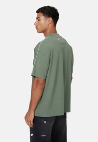 T-shirt verde oversize in cotone con maniche corte, colletto girocollo a coste e un design discreto sul retro, abbinato a jeans neri strappati.