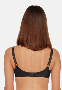 Schwarzer BH mit verstellbaren Trägern, nahtlosem Design und Haken- und Ösenverschluss auf der Rückseite. Weicher Stoff, minimalistische Ästhetik.