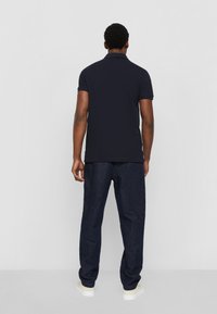 Polo shirt nella tonalità navy con maniche corte, colore uniforme e colletto piatto, abbinato a pantaloni in denim blu scuro e sneakers bianche.