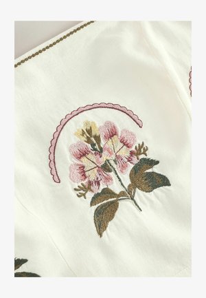 Fehér szövet, amely rózsaszín, sárga és zöld virágos hímzéssel díszített, a virágok felett hullámos rózsaszín szegéllyel.