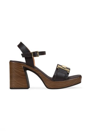 Sandalia de piel negra con puntera abierta, tacón bloque de madera, correa en el tobillo con hebilla dorada y adornos dorados decorativos en la correa frontal.