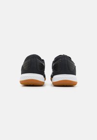 Scarpe sportive nere con tessuto testurizzato, dotate di una intersuola bianca e di una suola in gomma color caramello. La vista posteriore mostra dettagli cuciti e un design bicolore.