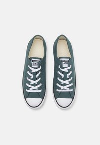 Baskets en toile verte avec lacets blancs, embout en caoutchouc et bordure noire. Elles disposent d'une semelle intérieure texturée et d'un patch logo classique sur la languette.